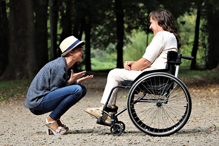 Young woman kneeling and talking to woman in a wheelchair