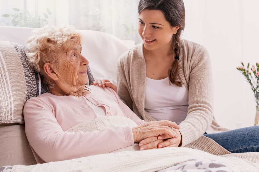 Young Adult Child Supporting Sick Parent Lying in Hospital Bed