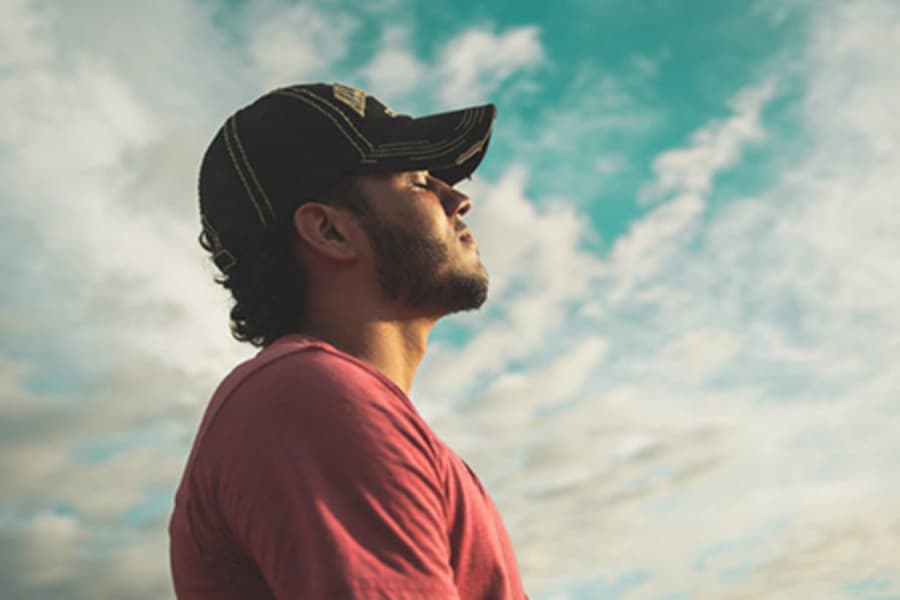 Man with hat under clouds experiencing serenity